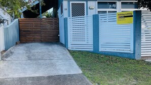 A gated property with a wooden fence and a metal gate, a concrete driveway, and a grassy area. - The Osprey House - Quaint 2 bedroom cottage in the centre of town (SOUTH WEST ROCKS)