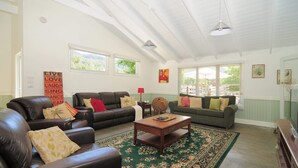 A spacious living room with leather sofas, a wooden coffee table, and a green patterned rug. There are two windows with blinds, a ceiling fan, and a wall with motivational quotes. - Spring Grove Dairy - Picturesque views! (Kangaroo Valley)