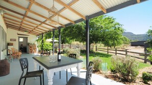 An outdoor covered patio with a table and chairs, a bottle of wine, and a view of a fenced pasture and trees. - Spring Grove Dairy - Picturesque views! (Kangaroo Valley)