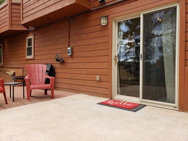 A wooden house exterior with a sliding glass door, a red Adirondack chair, and a 'hello' mat at the entrance. - Spacious, Comfortable and Clean Mountain Stay! (Woodland Park)