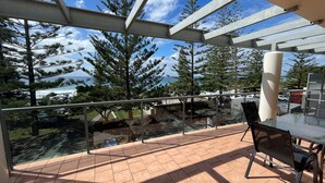 Ein Balkon mit Glastrennwand, Gartenmöbeln und Blick auf das Meer und Bäume.