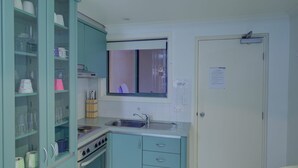 Eine kompakte Küche mit taubenblauen Schränken, einem Herd, einer Spüle und einem Fenster mit Jalousien.