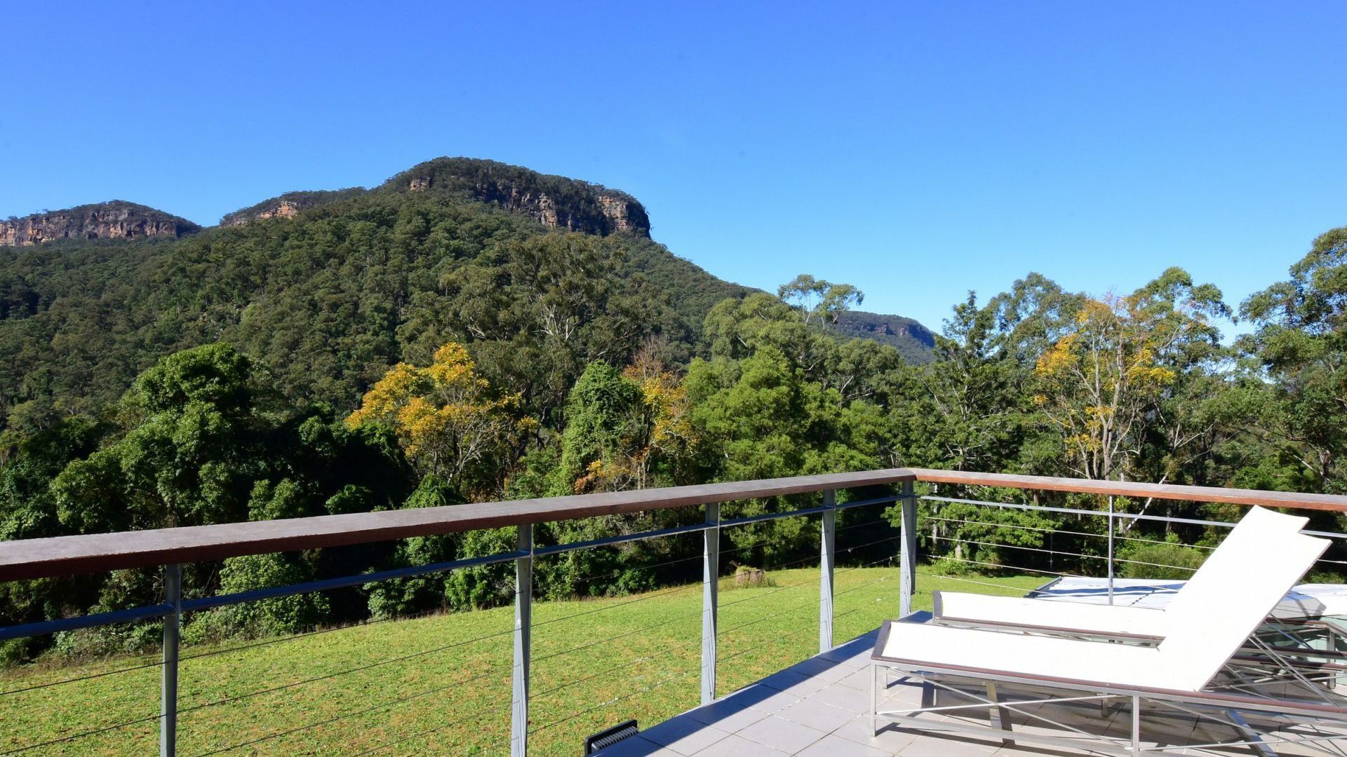 Eine Terrasse mit Geländer, die auf eine Wiese und einen bewaldeten Berg blickt.