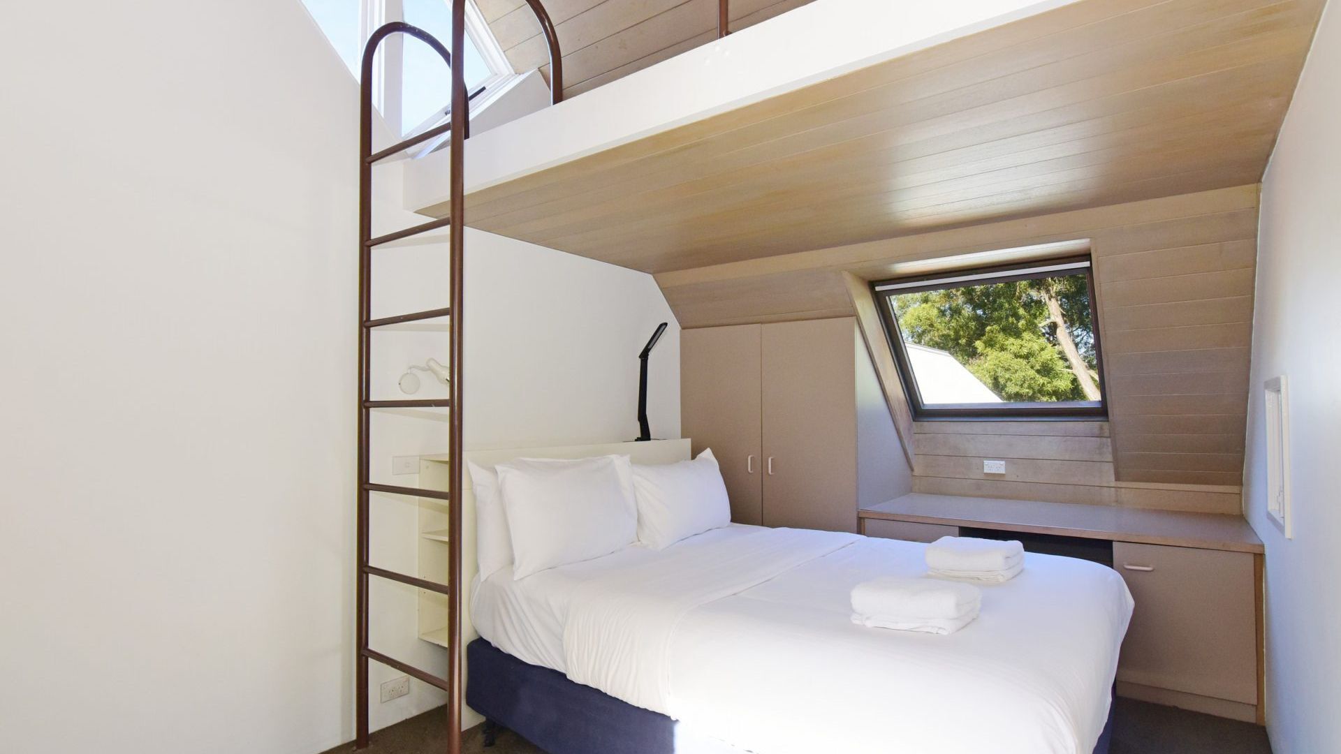 Quarto com beliche, claraboia e vista para árvores.
