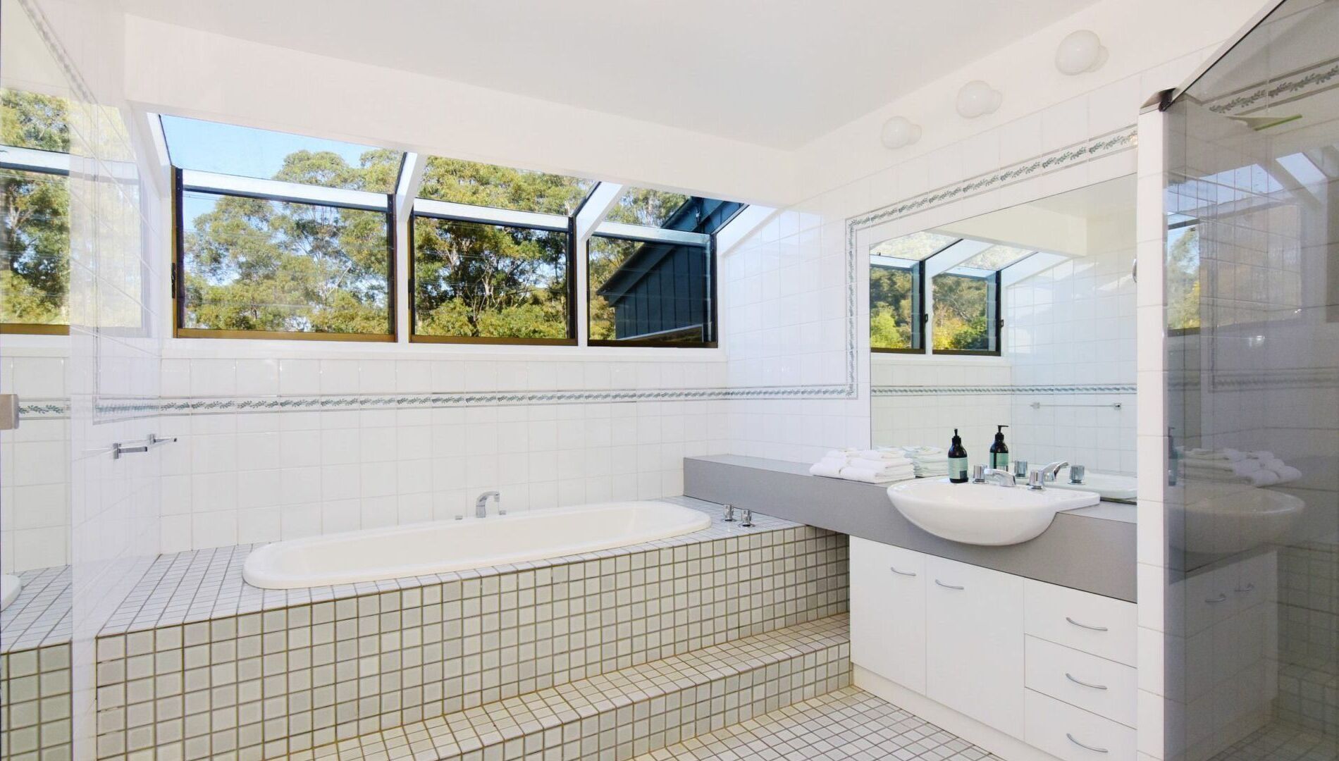 A modern bathroom with a freestanding bathtub, a large mirror, and a window with a view of trees.