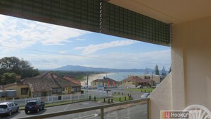 A balcony with a view of a beach, a parking lot, and buildings in the background.