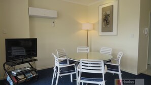 A room with a round table, white chairs, a flat-screen TV, a bookshelf, and a lamp.