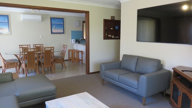 Een woonkamer met een grijze bank, een eettafel met stoelen, en een keuken die zichtbaar is door een open doorgang.