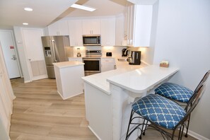 Una cocina moderna con armarios blancos, electrodomésticos de acero inoxidable y una isla central con taburetes de bar.