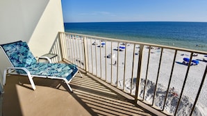 A balcony with a view of a beach, a lounge chair, and a small table. - Beachfront condo with multiple beach views (Gulf Shores)