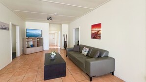 Un salon avec un canapé gris, une table basse noire et un téléviseur posé sur un meuble.