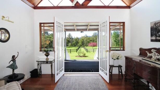 A room with a wooden floor, a white door leading to a garden, a small table with a vase, and a statue on the left.