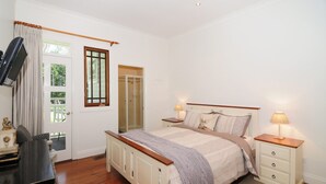 A bedroom with a bed, bedside tables, a TV, and a door leading to a balcony.