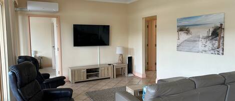 A living room with a flat-screen TV, leather sofas, a wooden cabinet, and a beach-themed painting.