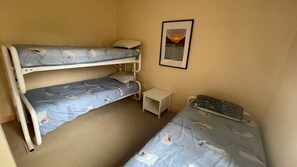 A room with two bunk beds, a small bedside table, and a framed picture on the wall.