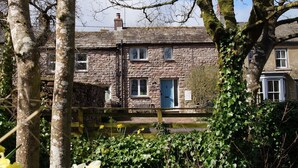 Une maison en pierre avec une porte bleue, entourée de verdure et de jonquilles.