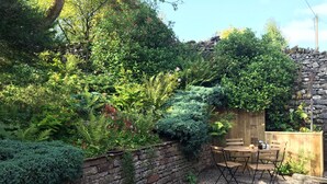 Un jardin avec un mur de pierre, une clôture en bois et une table avec des chaises.