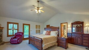 A bedroom with a wooden bed, a red chair, a dresser, a mirror, and a ceiling fan. - The Perch - 3 BR, 3 BA One Level Home, Panoramic Long-Range Mountain View (Waynesville)