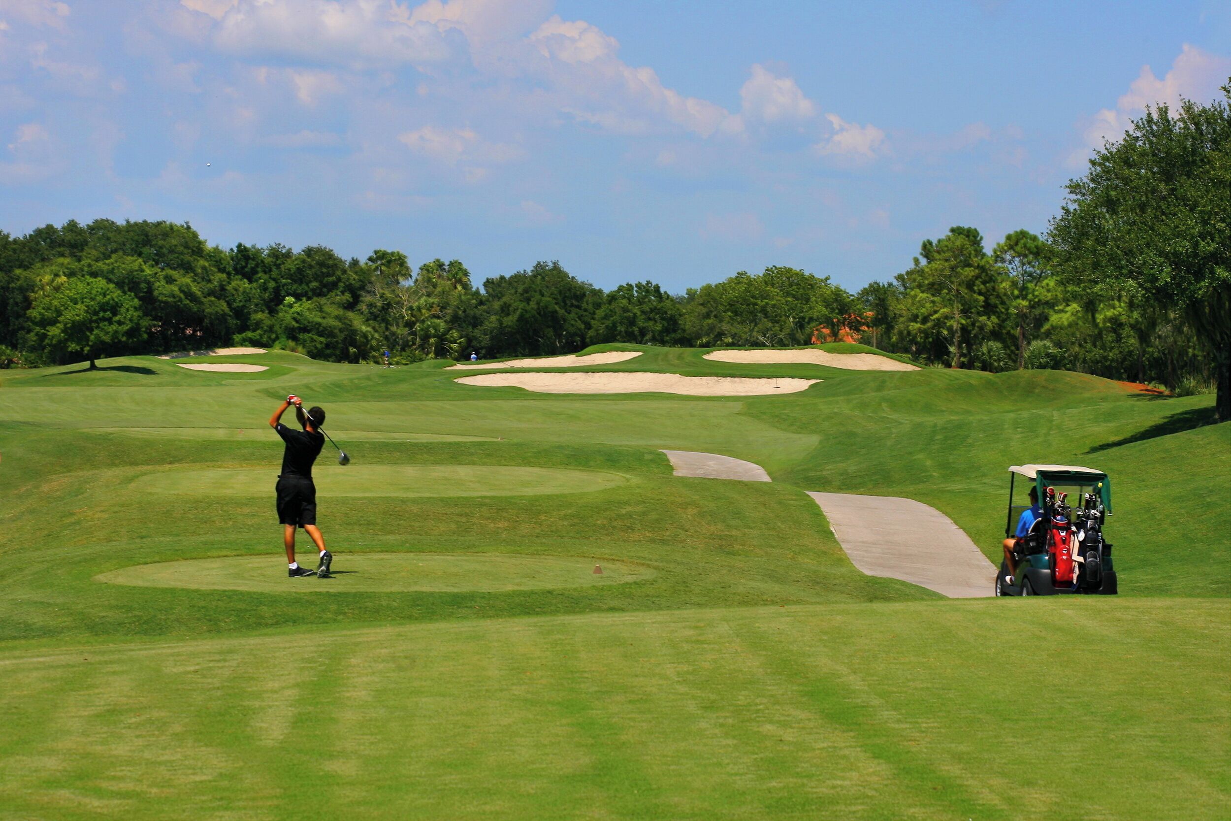 A golf course with a golfer in mid-swing, sand bunkers, and a golf cart.
