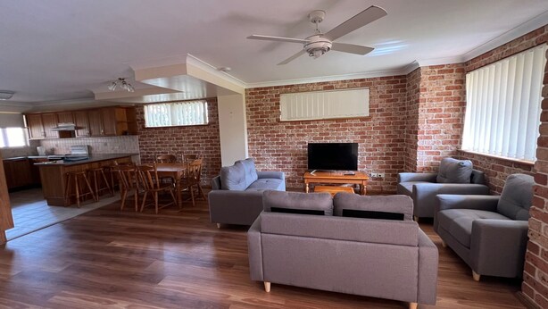 A living room with a fireplace, a dining area with a kitchen in the background, and a TV on a wooden table. - CARRINGTON TERRACE 4 - CLOSE TO FRONT CREEK BEACH ACCESS (South West Rocks)