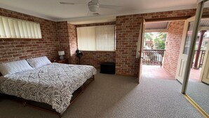 A bedroom with a brick wall, a bed with a patterned bedspread, a bedside table with a lamp, a fan, and a window with blinds. - CARRINGTON TERRACE 4 - CLOSE TO FRONT CREEK BEACH ACCESS (South West Rocks)