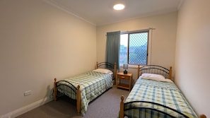 A small room with two single beds, a window with curtains, and a nightstand. - POINT BRINER 4 - MAIN BEACH VIEWS, SINGLE LOCK UP GARAGE (South West Rocks)