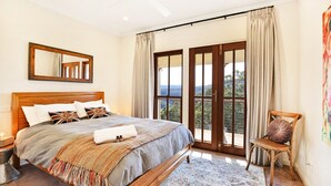 A bedroom with a large bed, a wooden headboard, a mirror, a chair, and a view through a glass door.