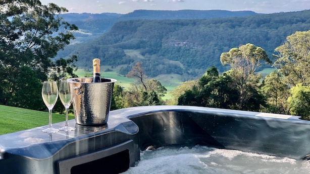 A hot tub with a champagne bottle and glasses, overlooking a scenic valley.