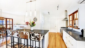 A modern kitchen with a central island, bar stools, pendant lighting, and a view of the outdoors.