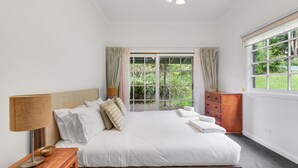 A bedroom with a bed, a bedside table with a lamp, a dresser, and a window with curtains. - Alcheringa Cottage - Amazing location with views! (KANGAROO VALLEY)