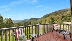 A balcony with two chairs and a table, overlooking a hilly landscape. - Alcheringa Cottage - Amazing location with views! (KANGAROO VALLEY)
