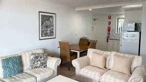 A living room with two sofas, a dining table with chairs, a refrigerator, and a fire extinguisher. - Little Ripple- Perfect couple retreat (South West Rocks)