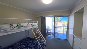 A room with bunk beds, a sliding glass door to a balcony, and a small table. - OCEANSHORES 18 LOVELY THREE BEDROOM UNIT CLOSE TO TOWN (SOUTH WEST ROCKS)
