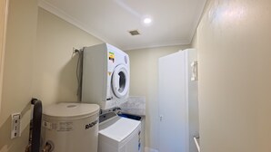 A laundry room with a washing machine, dryer, and a large container labeled 'RADIANT.' - OCEANSHORES 18 LOVELY THREE BEDROOM UNIT CLOSE TO TOWN (SOUTH WEST ROCKS)