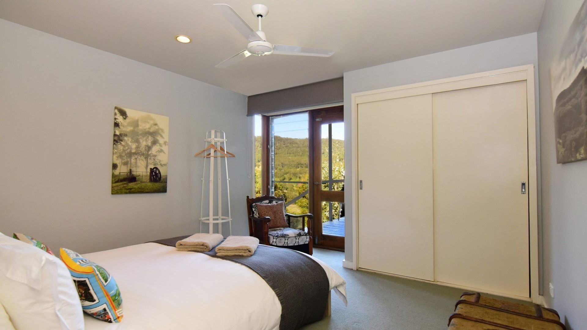 A bedroom with a bed, a chair, a wardrobe, and a view of the outdoors.