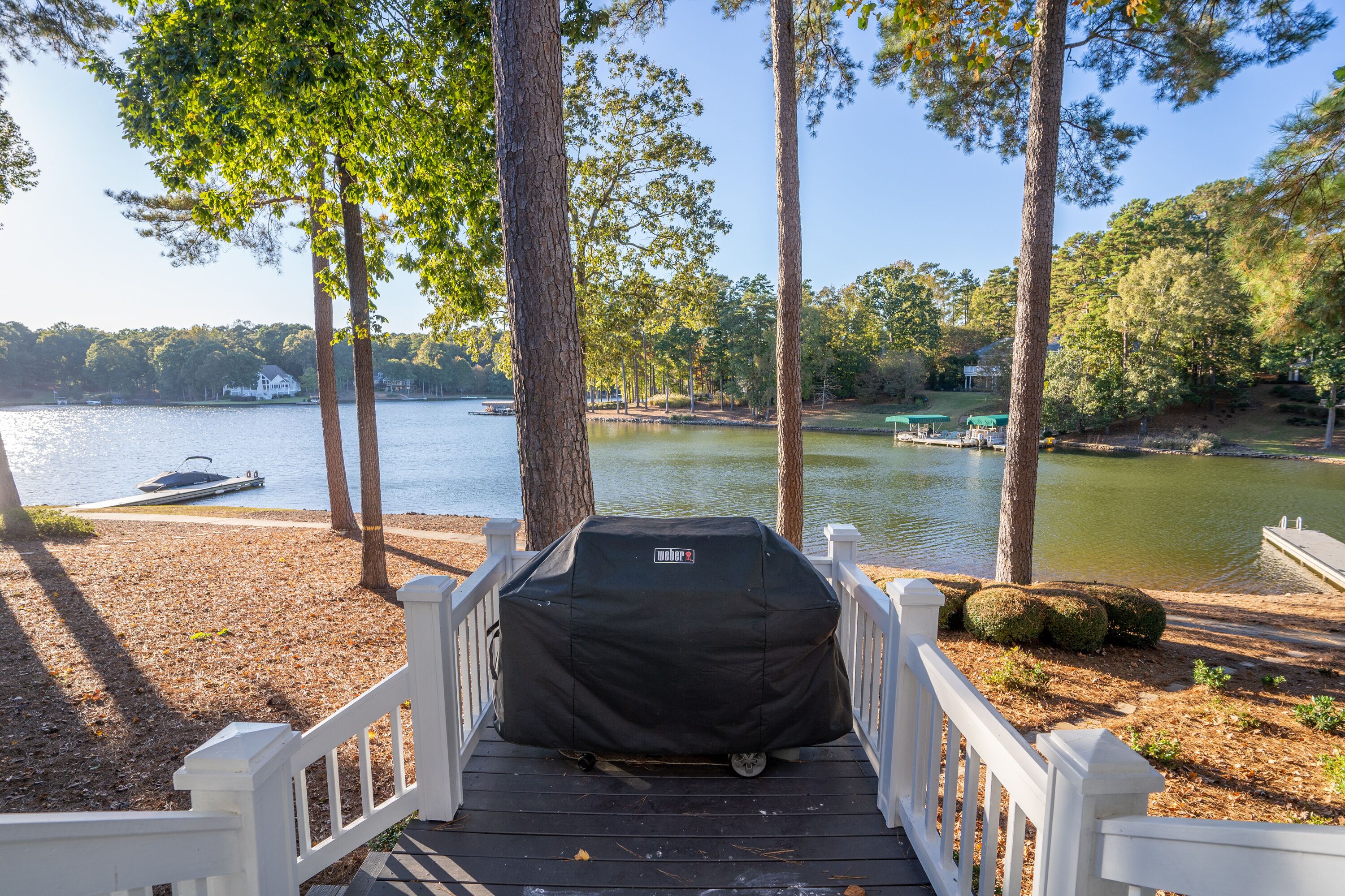 A deck with a grill cover, overlooking a lake with boats and trees.