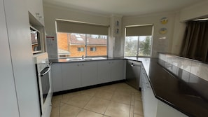 A kitchen with a window, a dishwasher, and a tiled floor. - Ocean Shores 16 (South West Rocks)