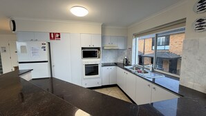 A modern kitchen with white cabinets, a microwave, oven, and a sink with a window view. - OCEAN SHORES 16 - 50 METRES TO BEACH & POOL IN COMPLEX (South West Rocks)