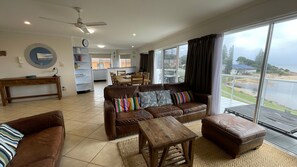 A spacious living area with a brown leather sofa, a wooden coffee table, and a view of a body of water through large windows.