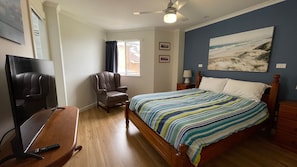 A bedroom with a bed, a chair, a desk with a computer, a ceiling fan, and a window with curtains. - Ocean Shores 16 (South West Rocks)
