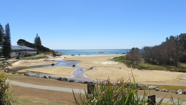 A beach with a building on the left, a clear sky, and a calm sea. - OCEAN SHORES 16 - 50 METRES TO BEACH & POOL IN COMPLEX (South West Rocks)