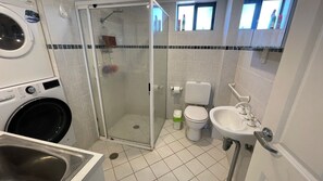 Un bany compacte amb plat de dutxa tancat per vidre, un vàter, un rentapous i una rentadora.