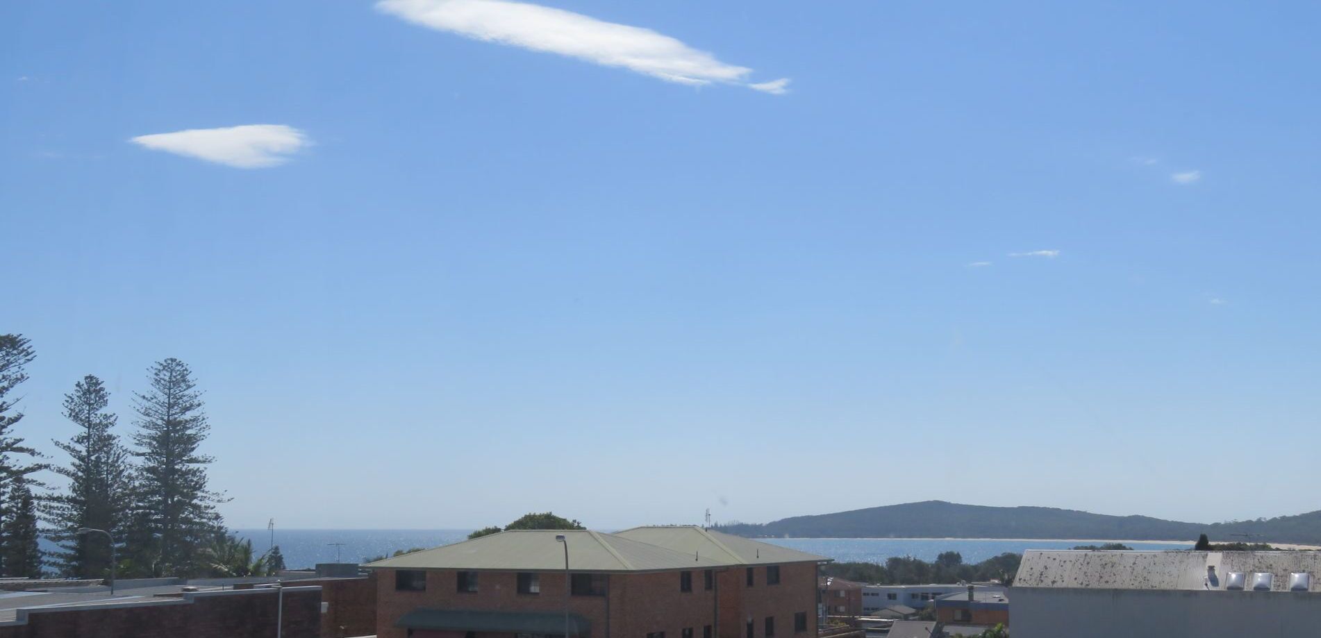 A building with a flat roof and a small antenna on top, surrounded by trees and a clear sky.