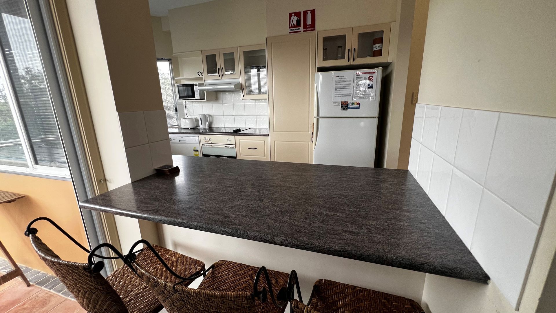 A kitchen with a granite countertop, white cabinets, a microwave, and a refrigerator.