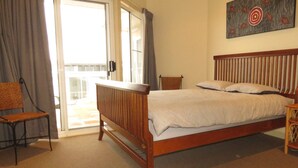 A bedroom with a wooden bed, a chair, a small table, and a painting on the wall. - SEABREEZE APARTMENTS UNIT 4 - AIRCONDITIONED CENTRE OF TOWN (South West Rocks)