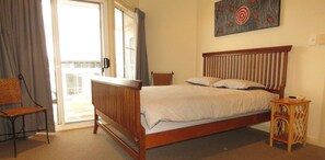 Un dormitorio con cama de madera, una silla, una mesita y un cuadro en la pared.