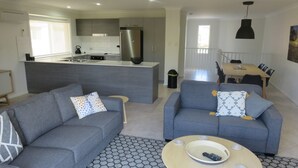 Un apartamento moderno con un sofá gris, una mesa de centro y una zona de cocina con refrigerador y fregadero.