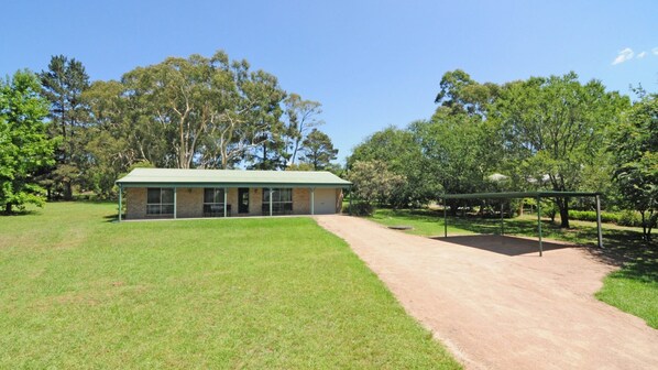 A building with a green roof, a covered patio area, and a dirt path leading to it.