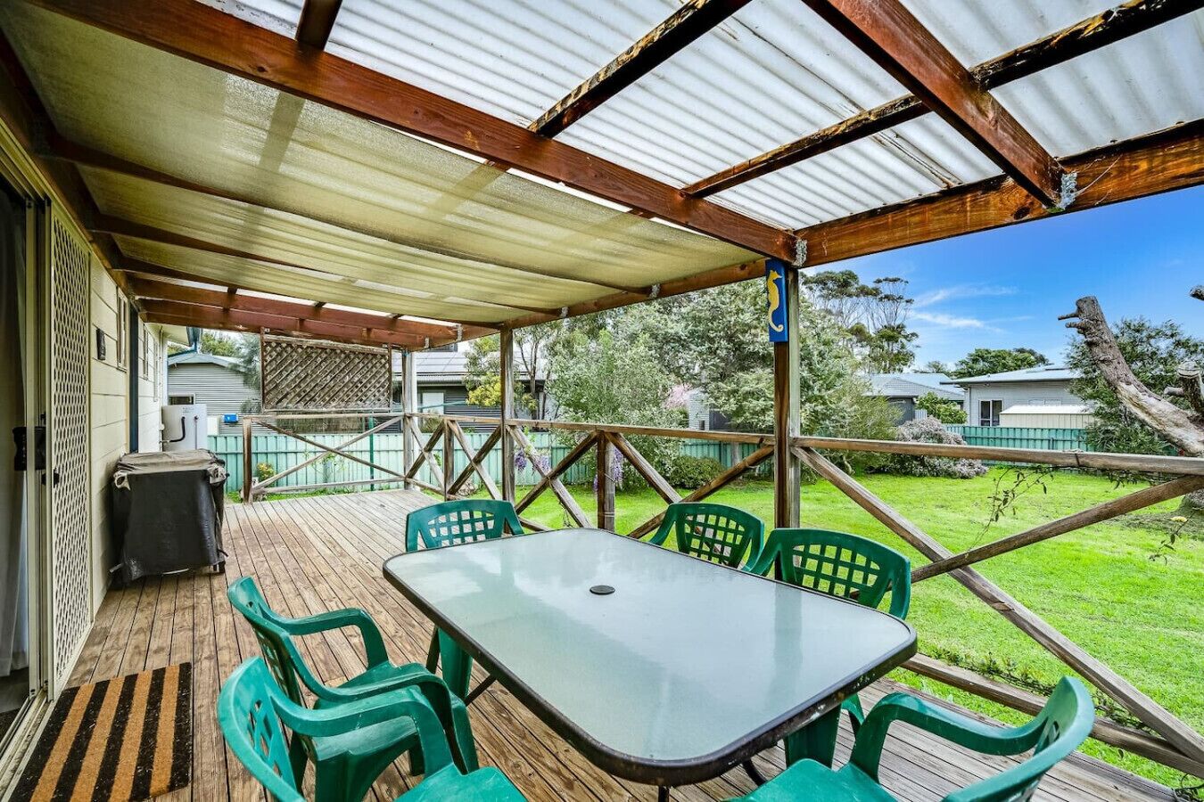 A covered outdoor area with a table and chairs, a wooden deck, and a view of the surrounding greenery.