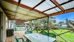Un espacio al aire libre techado con una mesa y sillas, una terraza de madera y vistas al entorno verde.